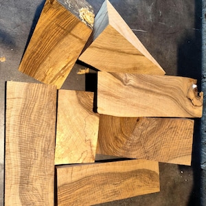 May include: Six pieces of wood with a natural wood grain pattern. The wood is light brown with darker brown streaks. The pieces are various shapes and sizes.