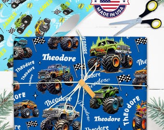 May include: Blue wrapping paper featuring colorful monster trucks, checkered flags, and the name "Theodore" in white. A "Made in USA" sticker and scissors are also visible. The paper is tied with twine and a wooden clip.