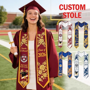May include: A maroon graduation gown and cap with a gold tassel. The graduate wears a custom stole with gold floral designs and the text "Class of 2026" and "Harvard University". Additional stoles with different designs are also shown.