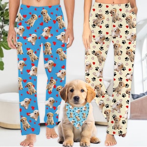 Peut inclure: Deux paires de pantalons de pyjama avec un motif de visage de chien et d'empreintes de pattes. Une paire est bleue avec des cœurs rouges et l'autre est crème avec des cœurs roses. Un chiot golden retriever porte un bandana bleu avec des empreintes de pattes.