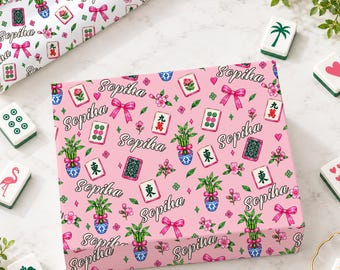 May include: A rectangular box with a pink background featuring a repeating pattern of the word Sopiha in black script, pink bows, green bamboo plants in blue and white pots, pink flowers, and various mahjong tiles with green and red symbols.