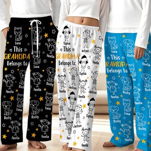 May include: Three pairs of pajama pants in black, white, and blue. Each pair features a repeating pattern of cartoon children, cats, dogs, and stars. The text "This Grandpa Belongs to" is printed in gold, with names below. The pants have a drawstring waist.