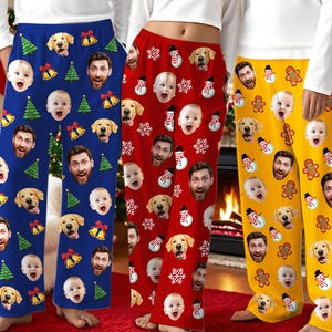May include: Three pairs of festive pajama pants in blue, red, and yellow. Each pair features a repeating pattern of faces, including a baby, a man, and a dog, along with Christmas-themed icons like trees, bells, snowmen, and gingerbread men.