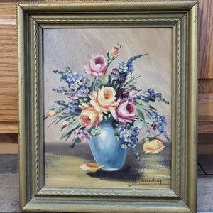 May include: A framed oil painting of a bouquet of flowers in a blue vase. The flowers are pink, yellow, and purple. The painting is signed "N.E. Greenleaf".