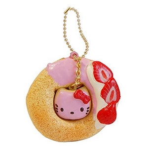 May include: A pink and white donut keychain with a strawberry topping and a Hello Kitty charm. The donut is made of a soft, squishy material.