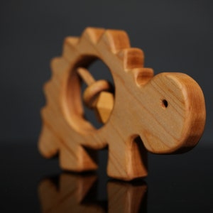 May include: Wooden toy dinosaur with a spinning rattle inside. The dinosaur is light brown and has a textured back.