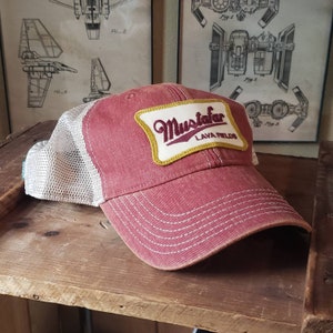 May include: A red and white trucker hat with a yellow and white patch that says "Mustafar Lava Fields".