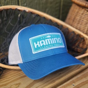 Peut inclure: Un chapeau de camionneur bleu et blanc avec un patch qui dit "2002 Kamino Cloning Tech" en texte blanc sur un fond turquoise.