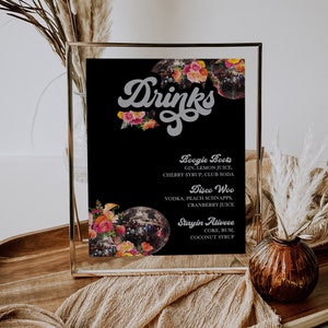 May include: A black framed sign with a disco ball and floral design. The sign lists three drink options: Boogie Boots, Disco Woo, and Stayin Aliveee. The text "Drinks" is written in a retro font.