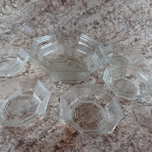 May include: A set of clear, vintage glass serving bowls. The bowls have an octagonal shape with textured detailing. The set includes a large bowl and several smaller bowls, perfect for serving snacks or desserts.