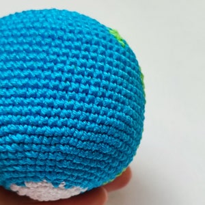 May include: A crocheted globe toy with blue, green, and white yarn. The globe is a sphere with a textured surface.