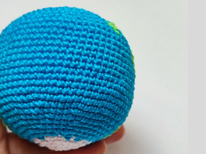 May include: A crocheted globe toy with blue, green, and white yarn. The globe is a sphere with a textured surface.