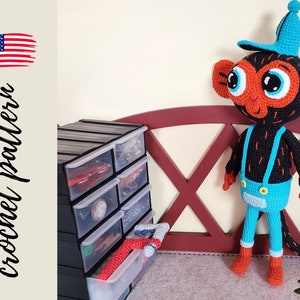 May include: Crochet pattern for a monkey wearing a blue and white baseball cap, blue overalls, and orange shoes. The monkey is standing on a red wooden bench with a black storage unit in the background.