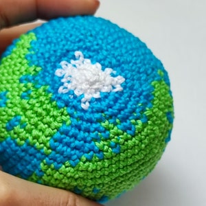 May include: A crocheted globe with green and blue yarn representing land and water. A white cloud is crocheted on the blue section.