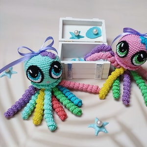 May include: Two crocheted octopus plushies with rainbow colored tentacles. The octopus on the left is turquoise with purple and yellow accents. The octopus on the right is pink with purple and green accents. Both have large black eyes and a bow.