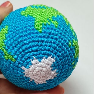 May include: A crocheted globe with blue, green, and white yarn. The globe is a sphere with a textured surface.