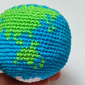 May include: A crocheted globe toy with blue and green yarn, representing the Earth. The globe is a sphere with a white center.