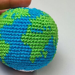 May include: A crocheted globe with blue and green yarn representing the Earth. The globe is white at the top and bottom.