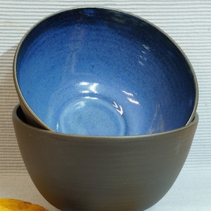 Könnte beinhalten: Ein Set aus drei Keramikbechern mit einer gesprenkelten, cremefarbenen Glasur. Jeder Becher hat ein anderes handgemaltes Blumendesign in Blau-, Grün- und Gelbtönen. Die Becher haben eine schlichte, moderne Form.