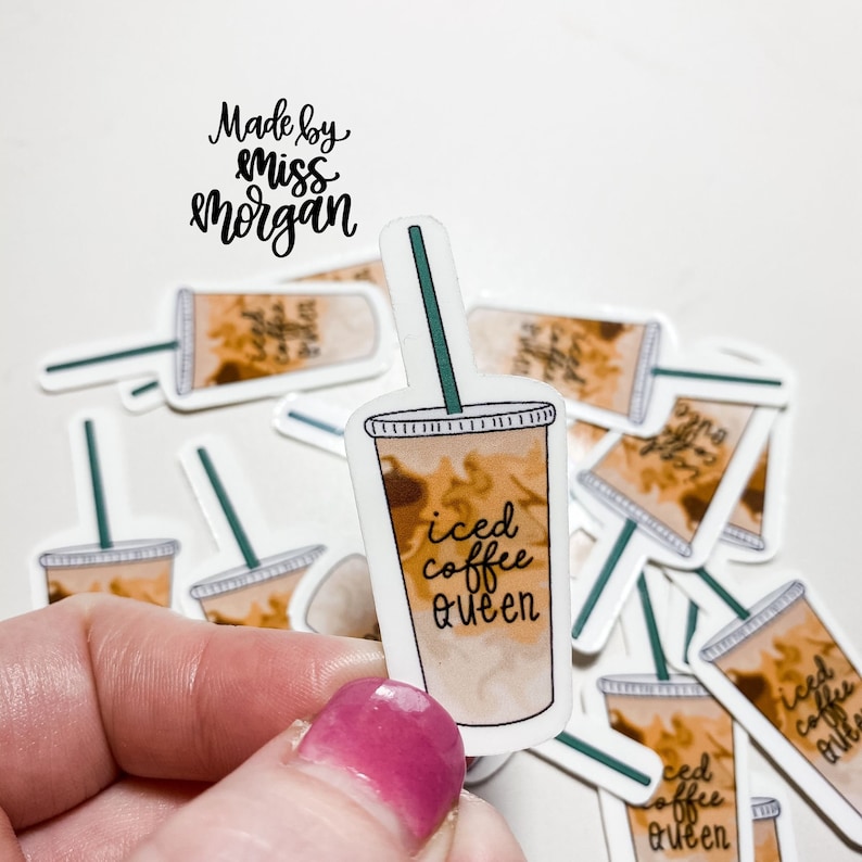 以下が含まれることがあります： 「iced coffee queen」というテキストが書かれた、漫画のアイスコーヒーカップが描かれたステッカーの束。ステッカーは白で、茶色と緑のアクセントが付けられている。「Made by Miss Morgan」というテキストが、画像の上部に黒の筆記体で書かれている。