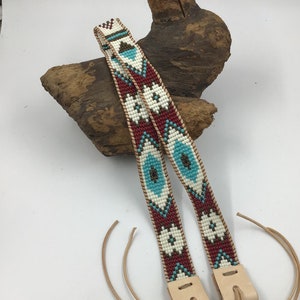 May include: Two beaded leather straps with a geometric pattern in white, red, turquoise, and brown. The straps are tied together with a knot at the end.