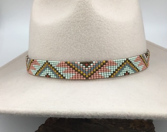 May include: A white felt fedora hat with a beaded band. The band is made of small, colorful beads in shades of pink, blue, brown, and yellow. The beads are arranged in a geometric pattern.