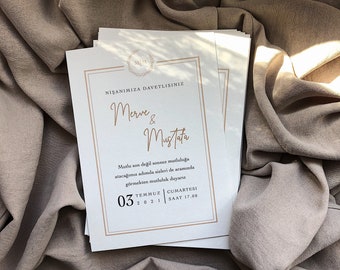 Può includere: Un invito di nozze bianco con lettere dorate che annunciano il fidanzamento di Merve e Mustafa. L'invito include la data e l'ora dell'evento: 3 luglio 2021 alle 17:00.