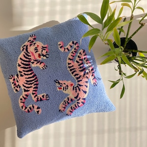 Könnte beinhalten: Ein blaues Kissen mit einem pinkfarbenen und schwarzen Tigerdesign. Das Kissen ist aus einem weichen, plüschigen Material.