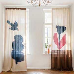 May include: Two off-white linen curtains featuring screen-printed designs. The left curtain displays a blue bird and a blue tree. The right curtain features a large blue and pink flower. Both curtains have a dark brown band at the top and bottom.