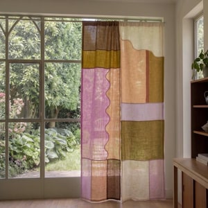 May include: A floor-length curtain panel featuring a patchwork design of rectangular and wavy-edged fabric sections in shades of mustard yellow, deep brown, light pink, lavender, and cream, hanging from a thin metal rod in front of a window.