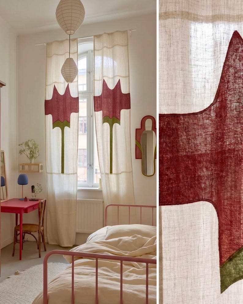 K&ouml;nnte beinhalten: Ein Paar cremewei&szlig;e Vorh&auml;nge mit einer gro&szlig;en, stilisierten roten Blumenapplikation mit gr&uuml;nem Stiel. Der Stoff weist eine sichtbare Webstruktur auf und das Design wiederholt sich auf beiden Bahnen, die an einer wei&szlig;en Stange vor einem Fenster h&auml;ngen.