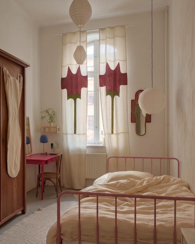 K&ouml;nnte beinhalten: Ein Schlafzimmer mit einem rosafarbenen Metallbettgestell und cremefarbener Bettw&auml;sche, einem Holzschrank mit einem h&auml;ngenden Kleidungsst&uuml;ck, einem rosafarbenen Schreibtisch mit Holzstuhl und bodenlangen cremefarbenen Vorh&auml;ngen mit Blumenapplikationen.