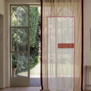 Puede incluir: Una cortina de cuerpo entero, semitransparente y de color blanco roto, con un borde burdeos oscuro en los lados verticales. La tela presenta un contorno rectangular rosa y un bloque horizontal sólido de color óxido en el centro.