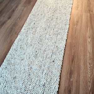 Handwoven wool jute runner rug in natural neutral tones, shown as a long narrow hallway runner with textured woven surface and optional fringes.