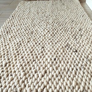 A long runner rug featuring a thick, chunky texture made from light beige/ off-white yarn with dark flecks. The rug displays a consistent, repeating braided pattern across its entire surface, creating a dense and tactile appearance.