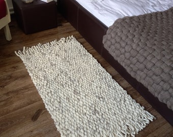 Peut inclure: Un tapis en tricot épais blanc et gris avec de longues franges sur un sol en bois. Le tapis est devant un lit en cuir marron avec une literie blanche et une couverture en tricot marron.