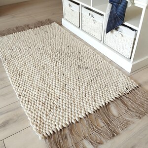A hallway  runner rug featuring a chunky, off-white handwoven texture with subtle dark flecks throughout.  The runner is made of natural undyed wool and jute and  is finished with long, natural-colored jute fringe along the two shorter ends, creating a tactile and layered appearance.