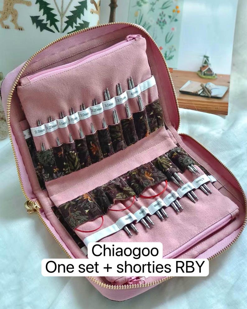 K&ouml;nnte beinhalten: Ein rosafarbenes Etui mit Rei&szlig;verschluss enth&auml;lt eine Sammlung von Stricknadelspitzen aus Metall und rote Kabel. Das Innere verf&uuml;gt &uuml;ber Stofff&auml;cher mit aufgedruckten Etiketten von 2,0mm bis 5,0mm. Text auf dem Bild: Chiaogoo One set + shorties RBY.
