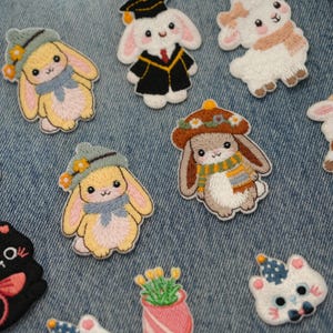 Op de afbeelding: Geborduurde patches met schattige konijntjes in verschillende outfits, waaronder hoeden en sjaals. De patches zijn in tinten geel, bruin en wit, met gedetailleerde steken. Perfect om kleding of accessoires een vleugje vrolijkheid te geven.