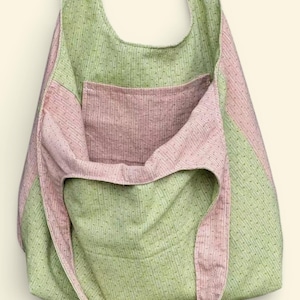 Pu&ograve; includere: Una grande borsa tote aperta con una tracolla. La borsa &egrave; realizzata in tessuto a righe verdi e rosa. La borsa ha una grande tasca sul davanti. La borsa &egrave; realizzata in un tessuto morbido e strutturato.
