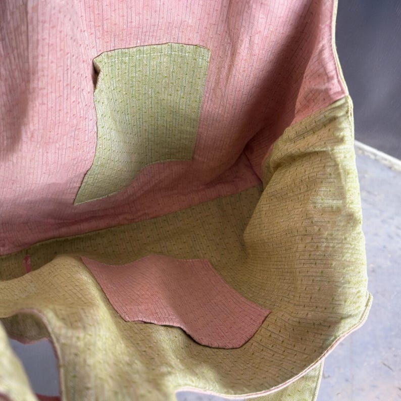 May include: Close-up of a handmade tote bag interior. The bag features a pink and green color scheme with a textured fabric. The interior has a pink lining with a green pocket. The exterior is green with a pink pocket.