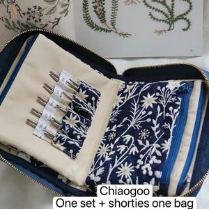K&ouml;nnte beinhalten: Ein dunkelblaues Stoffetui mit Rei&szlig;verschluss enth&auml;lt Stricknadelspitzen aus Metall, die in wei&szlig;en F&auml;chern organisiert sind. Das Innere zeigt ein Blumenmuster auf dunkelblauem Grund und eine Rei&szlig;verschlusstasche. Text: Chiaogoo One set + shorties one bag (Red/blue/yellow).