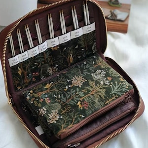 May include: A brown zippered knitting needle case, open to reveal various knitting needles and storage pockets. The case includes needles in sizes US 2 (2.75mm) to US 9 (5.5mm). The interior features a forest-themed fabric design.