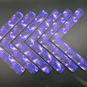 May include: Seven V-shaped decorative pieces with a marbled design in shades of blue, purple, and gold. The pieces are arranged in a row, with the points facing the same direction. The edges are white.