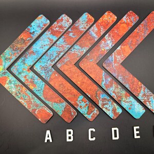 May include: Six L-shaped decorative pieces with a weathered, textured appearance. The pieces feature a mix of orange, blue, and brown colors, resembling aged metal. White letters A through F are placed below the pieces.