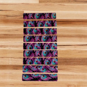 May include: Ten strips of adhesive tape with a peacock feather pattern. The feathers are pink, blue, and black on a dark background.