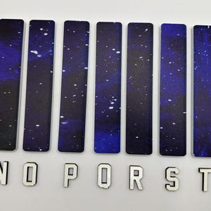 May include: A set of ten rectangular bookmarks with a dark blue and purple galaxy design, interspersed with white star-like specks. Below the bookmarks are the letters M, N, O, P, R, S, T, and U in a white, blocky font.