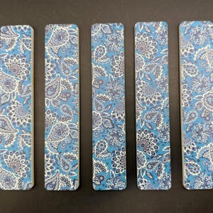May include: Five rectangular bookmarks with a blue paisley floral pattern. The design features white and navy blue floral and paisley elements on a light blue background. The bookmarks are arranged vertically.