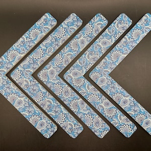 May include: Six blue paisley print boomerang-shaped items arranged in a chevron pattern. The fabric features a detailed floral design in shades of blue, white, and gray. The items are likely decorative or functional.
