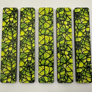 May include: Five rectangular bookmarks with a vibrant leaf design. The leaves are rendered in shades of green and yellow, with black outlines. The bookmarks are arranged vertically, showcasing the intricate pattern.